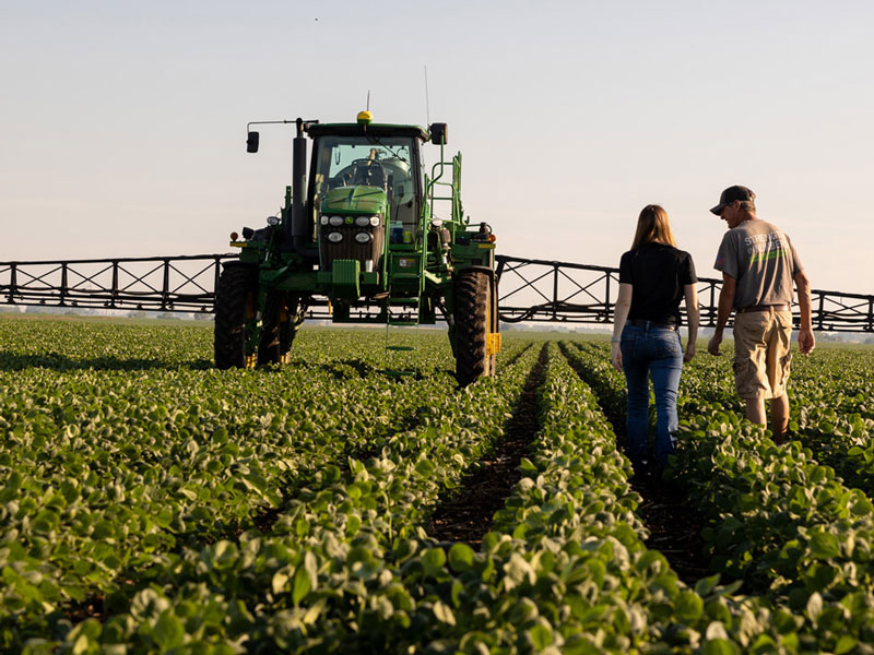 Photo of 2 farmers walking in field toward sprayer